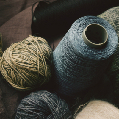 an assortment of spools and balls of blue, grey and earthy colored yarns, twines and thread